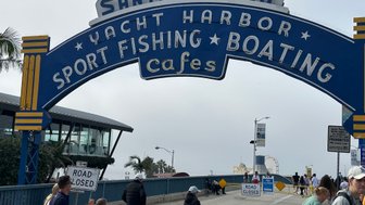 Der ikonische Santa Monica Schriftzug über dem Hafen, umgeben von Menschen, die die Küstenatmosphäre genießen.