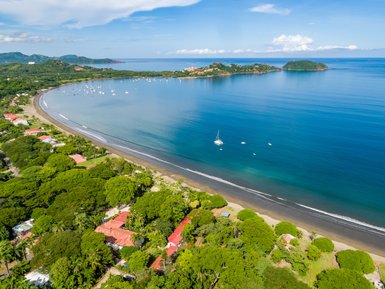 Eine atemberaubende Küstenansicht mit sanften Wellen, Booten im Wasser und üppigem Grün entlang des Strandes.