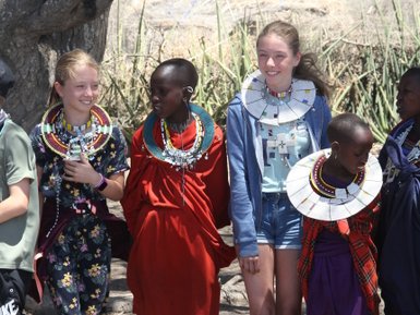 Zwei Mädchen stehen zusammen mit Massai-Leuten in traditioneller Kleidung – Tansania Reise mit Kindern