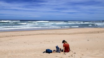 Kind sitzt mit Mutter im Sand und schaut aufs Meer – Garden Route Familienreise