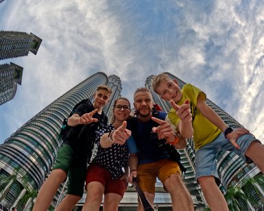 Familie posiert fröhlich für ein Selfie mit den Petronas Twin Towers im Hintergrund – Malaysia & Borneo Reise mit Kindern