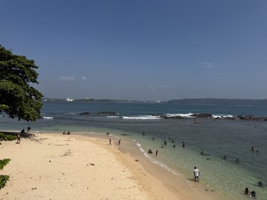 Ein sonniger Strand mit feinem Sand, wo Menschen im Wasser schwimmen und am Ufer entspannen.
