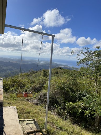 Ein Kind schwingt auf einer Schaukel mit Blick auf eine atemberaubende Landschaft und einen klaren blauen Himmel.