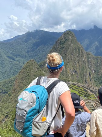Eine Gruppe von Menschen steht auf einem Aussichtspunkt und bewundert die Ruinen von Machu Picchu inmitten der Berge.
