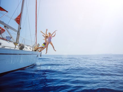 Drei Kinder springen fröhlich von einer Yacht ins glitzernde blaue Wasser, umgeben von einem klaren Himmel.