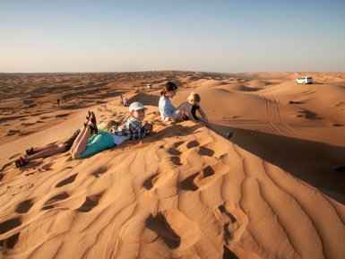 Kinder sitzen gemeinsam auf einer Wüstendüne – Oman Familienreise
