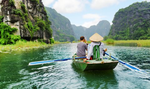 Zwei Personen sitzen in einem Boot und genießen die ruhige Landschaft mit hohen, bewaldeten Klippen im Hintergrund.