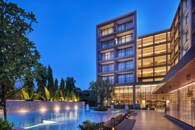 Ein elegantes Hotelgebäude mit beleuchteten Balkonen, umgeben von üppigem Grün und einem glitzernden Pool bei Dämmerung.
