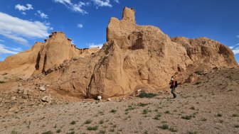 Ein Wanderer erkundet die beeindruckenden, sandfarbenen Felsformationen unter einem strahlend blauen Himmel in der Mongolei.