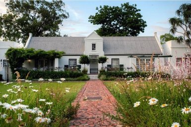 Ein charmantes Cottage mit einem begrünten Garten, umgeben von bunten Blumen und einem gepflasterten Weg.