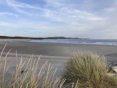 Ein ruhiger Strand mit sanften Wellen, umgeben von sanften Hügeln und Gras, das im Wind weht.