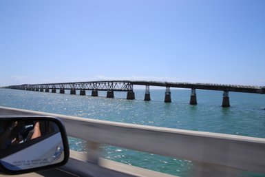 Eine lange Brücke erstreckt sich über das glitzernde Wasser, während ein Auto auf der Straße daneben fährt.