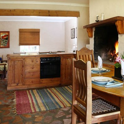 Eine gemütliche Küche mit Holzregalen, einem Esstisch und einem offenen Kamin, der eine warme Atmosphäre schafft.