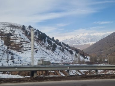 Schneebedeckte Hügel erstrecken sich unter einem klaren Himmel, während majestätische Berge im Hintergrund sichtbar sind.
