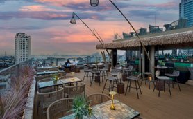 Eine stilvolle Dachterrasse mit modernen Möbeln, umgeben von Pflanzen und einem atemberaubenden Sonnenuntergang über der Stadt.