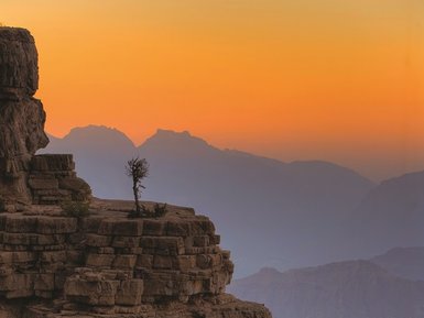 Die Sonne geht über dem Canyon unter und taucht die Felswände in warmes Licht – Oman Reise mit Kindern