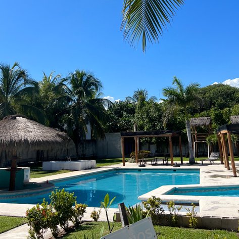 Ein klarer blauer Himmel über einem einladenden Pool, umgeben von üppigen Palmen und einem schattigen Strohdach.