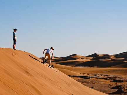 Kinder haben Spaß beim Sandboarding auf den goldenen Dünen – Familienreise mit Kindern