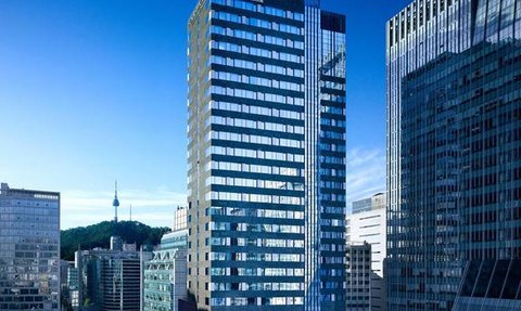 Das moderne Gebäude des Four Points Hotels in Seoul erhebt sich zwischen anderen Wolkenkratzern unter einem klaren blauen Himmel.