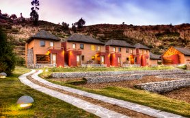 Die malerische Lodge mit strohgedeckten Dächern liegt in einer sanften Hügellandschaft, umgeben von üppigem Grün.