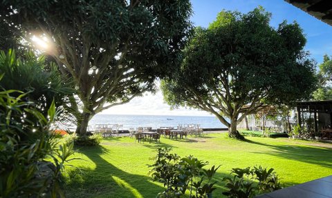 Großzügiger Garten mit einer schönen Aussicht auf das Wasser, umgeben von hohen Bäumen und entspannenden Terrassenmöbeln.