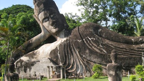 Eine massive, liegende Buddha-Statue dominiert den Park, umgeben von üppigem Grün und weiteren kleineren Statuen.