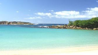 Ein ruhiger Strand mit feinem, hellem Sand und klarem, türkisfarbenem Wasser unter einem strahlend blauen Himmel.