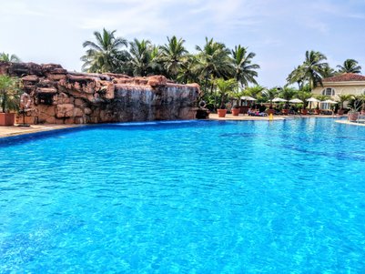 Ein glitzernder Pool mit klarem, blauem Wasser, umgeben von Palmen und einer Felswand mit Wasserfall im Hintergrund.
