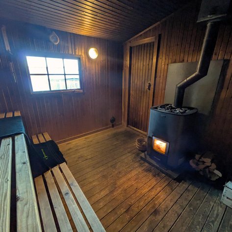 Eine gemütliche Sauna mit Holzbank, einem Ofen und einem Fenster, das Tageslicht hereinlässt.