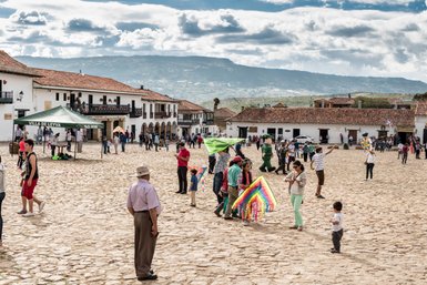 Ein belebter Platz in Villa de Leyva, wo Menschen fröhlich mit bunten Drachen spielen und die Sonne scheint.