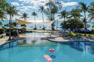 Ein einladender Poolbereich mit Palmen, Liegen und Sonnenschirmen, der einen Blick auf das glitzernde Meer bietet.