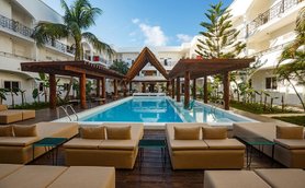 Ein einladender Poolbereich mit modernen Liegen und einem schattigen Pavillon, umgeben von tropischen Pflanzen und klarem Himmel.