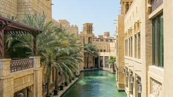 Ein malerischer Kanal in der Altstadt von Dubai, umgeben von traditionellen Gebäuden und Palmen unter klarem Himmel.
