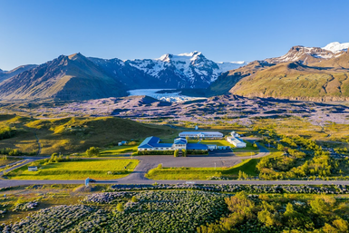 Eine weitläufige Landschaft mit einem Hotel im Vordergrund, umgeben von grünen Wiesen und majestätischen Bergen im Hintergrund.
