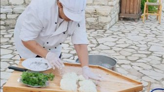 Eine Person in Kochkleidung bereitet frischen Halloumi-Käse auf einem Holztisch im Freien vor.