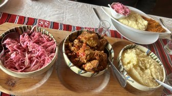 Ein rustikales Essen mit buntem Rotkohl, zartem Fleisch und cremigem Püree auf einem Holzbrett serviert.