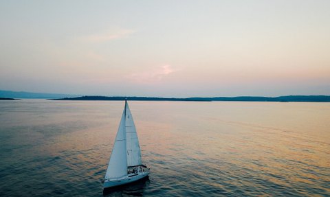 Ein Segelboot gleitet sanft über das ruhige Wasser, während der Himmel in sanften Pastellfarben leuchtet.