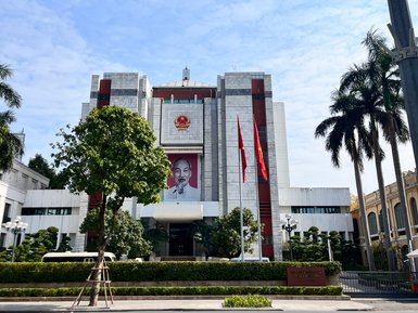 Ein modernes Gebäude mit einer großen Porträtaufnahme von Ho Chi Minh, umgeben von grünen Pflanzen und Flaggen.