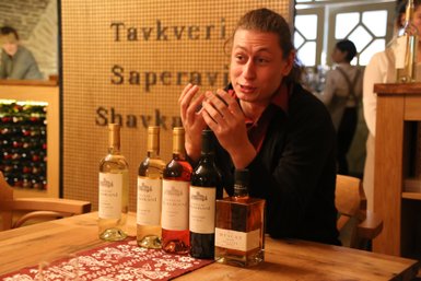 Ein Mann erklärt leidenschaftlich verschiedene Weinsorten, während Flaschen auf einem Holztisch stehen.