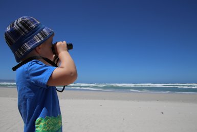 Ein Kind beobachtet aufmerksam das Meer mit Ferngläsern am Grotto Beach in Hermanus – Südafrika mit Kindern