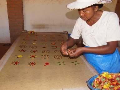 Eine Frau arbeitet sorgfältig an der Herstellung von handgefertigtem Papier, umgeben von bunten Blumenmustern.