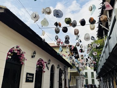 Bunte Hüte hängen über einer lebhaften Straße in der Altstadt, umgeben von charmanten, historischen Gebäuden.