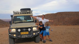 Eine Mutter steht mit ihren beiden Söhnen neben einem Jeep - Namibia Rundreise mit Kindern
