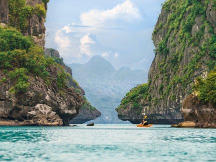 Ein Kajakfahrer paddelt durch die ruhigen Gewässer von Halong Bay, umgeben von beeindruckenden Felsen und üppiger Vegetation.