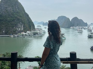 Eine Frau in einem blauen Kleid steht an einem Geländer und blickt auf die beeindruckende Halong-Bucht mit ihren Felsen.