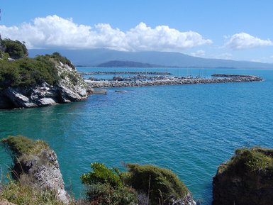 Eine malerische Küstenlandschaft mit klarem, blauem Wasser und sanften Wellen, umgeben von grünen Hügeln.