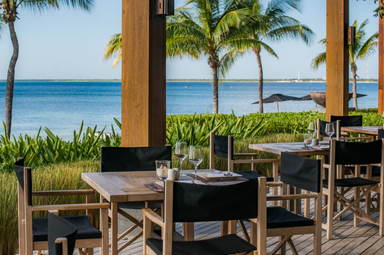 Ein eleganter Essbereich im Freien mit Blick auf das ruhige Wasser und Palmen, ideal für entspannte Mahlzeiten.