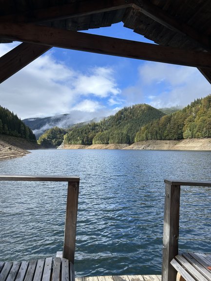 Ein Blick auf einen ruhigen See, umgeben von bewaldeten Hügeln und einem klaren blauen Himmel mit einigen Wolken.