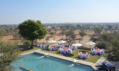 Ein Blick auf den Pool des Hotels Mandawa Haveli, umgeben von eleganten Tischen und Sonnenschirmen im Freien.