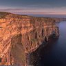 Die beeindruckenden Cliffs of Moher erheben sich majestätisch über den ruhigen Atlantik, beleuchtet von warmem Abendlicht.